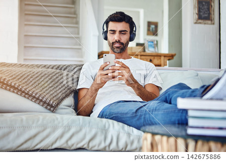 Man, phone and video with headphones on sofa for sound, audio and streaming service in living room with relax. Person, smartphone and mobile app for listening to music, radio and subscription in home 142675886