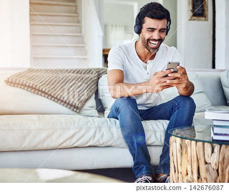 Man, headphones and laughing with phone in home for funny video, social media post and comedy movie on mobile app. Person, smartphone and happy for listening to audio, sound and subscription on couch Man, headphones and laughing with phone in home for funny video, social media post and comedy movie on mobile app. Person, smartphone and happy for listening to audio, sound and subscription on couch 142676087