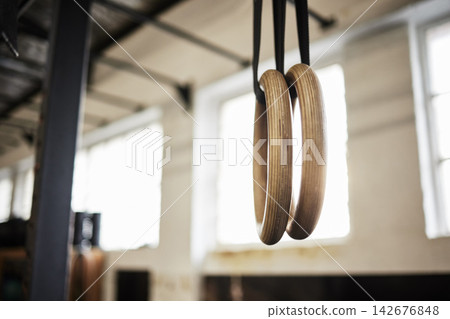 Rings, gymnastics and equipment for training in empty center for development for sports competition. Interior, gym and wood handles for balance, exercise and swing for tournament, contest or club Rings, gymnastics and equipment for training in empty center for development for sports competition. Interior, gym and wood handles for balance, exercise and swing for tournament, contest or club 142676848