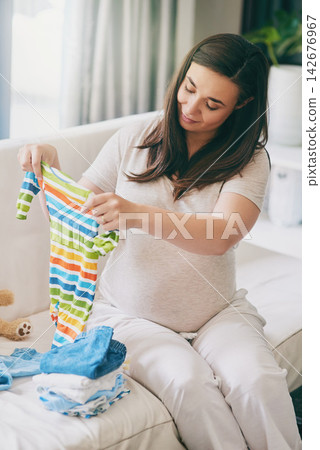 Pregnant, woman and smile with clothes on sofa for newborn attire or apparel, folding and organizing for arrival of baby. Mother to be, vest and garments for wardrobe in home and ready for motherhood 142676967