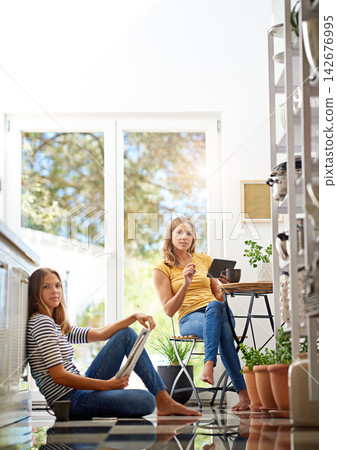 Relax, portrait and sisters in kitchen with coffee for morning bonding and happy relationship. Women, twins and weekend chat with newspaper, tablet and sitting together in home for social connection. Relax, portrait and sisters in kitchen with coffee for morning bonding and happy relationship. Women, twins and weekend chat with newspaper, tablet and sitting together in home for social connection. 142676995