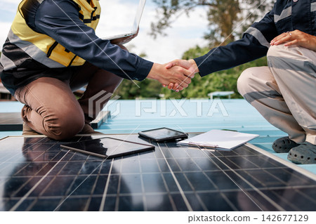 Two solar energy workers shake hands beside rooftop panels, with a tablet and paperwork a successful renewable power project. Two solar energy workers shake hands beside rooftop panels, with a tablet and paperwork a successful renewable power project. 142677129