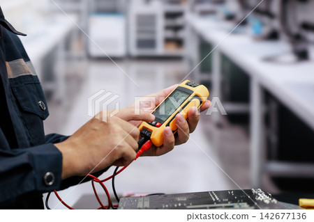 Close-up of a technician using a digital multimeter with test leads to check an electronic circuit board in a workshop. 142677136