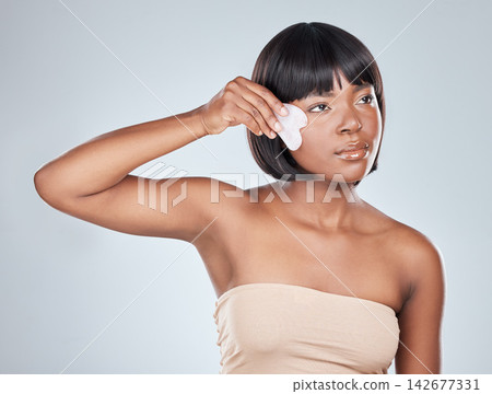 Gua Sha, beauty and black woman with cosmetics, skincare and dermatology in studio. Wellness, youth serum and rose quartz with facial massage, skin glow and care with calm and shine from treatment Gua Sha, beauty and black woman with cosmetics, skincare and dermatology in studio. Wellness, youth serum and rose quartz with facial massage, skin glow and care with calm and shine from treatment 142677331