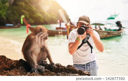 Man, camera and monkey with holiday, beach and tropical island with getaway trip, Bali and tourism. Person, photographer and tourist with equipment, seaside and memory with wild animal and sunshine Man, camera and monkey with holiday, beach and tropical island with getaway trip, Bali and tourism. Person, photographer and tourist with equipment, seaside and memory with wild animal and sunshine 142677392