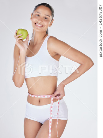 Woman, measuring tape and apple in studio portrait, tracking progress and white background. Female person, weight loss and results of liposuction or nutrition, cosmetic change and diet for health Woman, measuring tape and apple in studio portrait, tracking progress and white background. Female person, weight loss and results of liposuction or nutrition, cosmetic change and diet for health 142678307