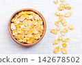 Sugar coated corn flakes, crispy breakfast cereal in a wooden bowl on linen fabric. Cornflakes, made from toasting flakes of corn, glazed with sugar. Enjoyed with milk, or eaten as a snack. Photo Sugar coated corn flakes, crispy breakfast cereal in a wooden bowl on linen fabric. Cornflakes, made from toasting flakes of corn, glazed with sugar. Enjoyed with milk, or eaten as a snack. Photo 142678502