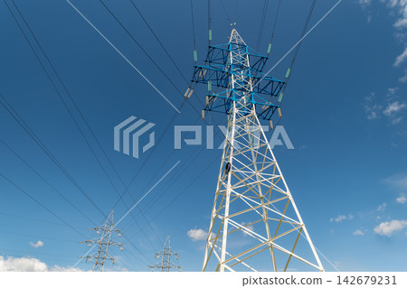 Tall power lines stretch towards the bright blue sky showcasing engineering marvels standing against fluffy white clouds Tall power lines stretch towards the bright blue sky showcasing engineering marvels standing against fluffy white clouds 142679231