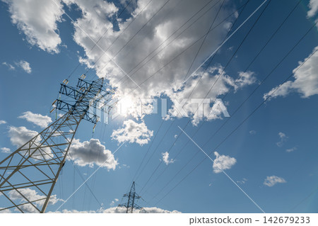 Power lines reach toward the vast blue sky while fluffy clouds drift elegantly on a sunny day Power lines reach toward the vast blue sky while fluffy clouds drift elegantly on a sunny day 142679233