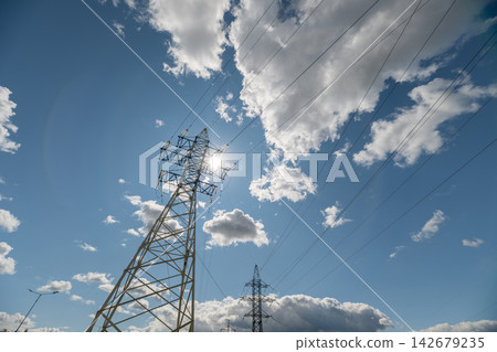 Dramatic clouds dance above towering electric pylons in a vibrant daylight sky Dramatic clouds dance above towering electric pylons in a vibrant daylight sky 142679235