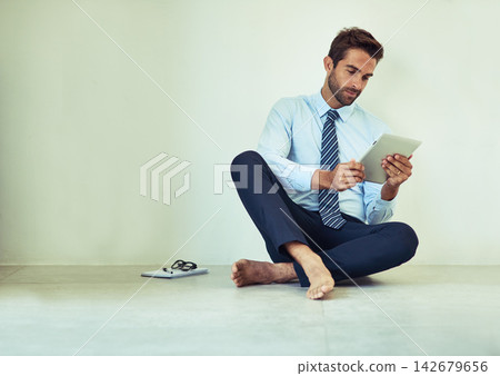 Business, man and relax with tablet on floor for reading online from digital technology. Male person, sitting and wall by surfing internet, browsing and research on wireless tech at home on ground Business, man and relax with tablet on floor for reading online from digital technology. Male person, sitting and wall by surfing internet, browsing and research on wireless tech at home on ground 142679656