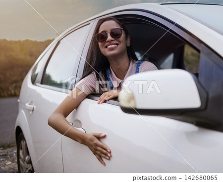 Woman, adventure and happy in car window with smile for travel or road trip with relaxing journey in summer. Weekend, holiday and stress relief with vacation or ride in countryside for view with calm Woman, adventure and happy in car window with smile for travel or road trip with relaxing journey in summer. Weekend, holiday and stress relief with vacation or ride in countryside for view with calm 142680065