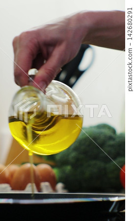 Vertical video. Woman pours oil on a frying pan on an electric stove. Modern kitchen appliance. Food preparation - pouring oil on frying pan. Vertical video. Woman pours oil on a frying pan on an electric stove. Modern kitchen appliance. Food preparation - pouring oil on frying pan. 142680291