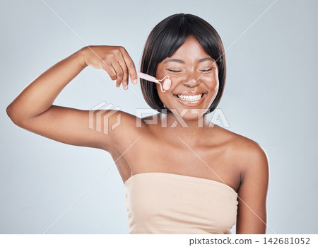 African woman, rose quartz roller and studio with smile for skin routine with natural glow by background. Girl, person and happy with stone, crystal or product for beauty, health and cosmetic change African woman, rose quartz roller and studio with smile for skin routine with natural glow by background. Girl, person and happy with stone, crystal or product for beauty, health and cosmetic change 142681052