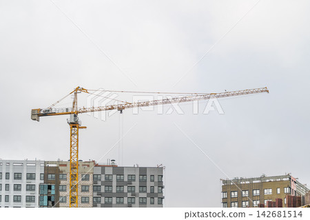 Construction site in the heart of the city with a towering yellow crane reaching towards the cloudy sky Construction site in the heart of the city with a towering yellow crane reaching towards the cloudy sky 142681514