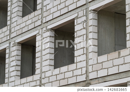 Construction project shows unfinished masonry work with empty window frames under a cloudy sky Construction project shows unfinished masonry work with empty window frames under a cloudy sky 142681665