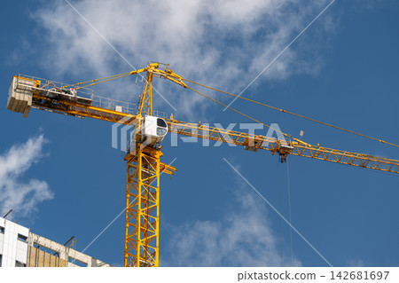 Construction crane towers over a bustling cityscape under a bright blue sky Construction crane towers over a bustling cityscape under a bright blue sky 142681697
