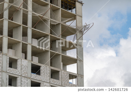 Construction of a modern building showcasing raw concrete and mesh netting against a vibrant sky Construction of a modern building showcasing raw concrete and mesh netting against a vibrant sky 142681726