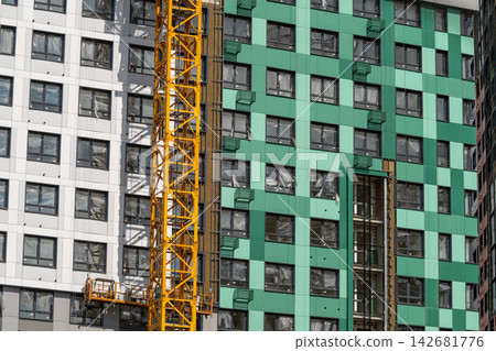 Brightly colored apartment building under construction with a yellow crane in a bustling urban area Brightly colored apartment building under construction with a yellow crane in a bustling urban area 142681776