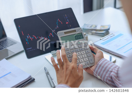 Investor checking stock market data on screen and calculating capital gains profit at desk. Investor checking stock market data on screen and calculating capital gains profit at desk. 142681846