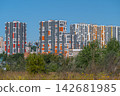 Modern high-rise buildings stand tall against the clear blue sky showcasing vibrant colors in a bustling city backdrop surrounded by nature 142681985