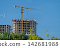 Construction workers build a tall building under a clear blue sky with a yellow crane in the background 142681988