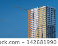 New skyscraper construction rises against a clear blue sky showcasing vibrant colors and modern architecture in a bustling city 142681990