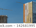 Construction of modern buildings showcasing cranes and vibrant architecture against a clear blue sky 142681995