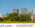 Modern skyline rises against a clear blue sky revealing vibrant apartments amidst greenery and construction in the foreground 142681997