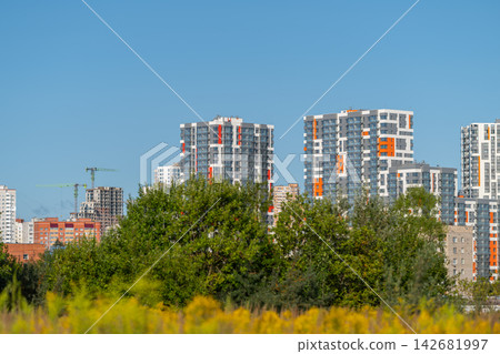 Modern skyline rises against a clear blue sky revealing vibrant apartments amidst greenery and construction in the foreground Modern skyline rises against a clear blue sky revealing vibrant apartments amidst greenery and construction in the foreground 142681997