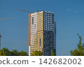 Construction progress on a vibrant high-rise building overlooking a blue sky with cranes actively working in the foreground 142682002