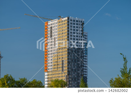 Construction progress on a vibrant high-rise building overlooking a blue sky with cranes actively working in the foreground Construction progress on a vibrant high-rise building overlooking a blue sky with cranes actively working in the foreground 142682002