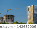 Bright blue skies loom over a bustling construction site with cranes busy at work showcasing a blend of new and old apartment buildings under development 142682006
