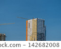 New building emerges against a clear sky cranes busy at work during midday construction in the heart of the city 142682008