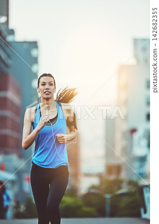 Woman, street and running for exercise with earphones, music streaming app and phone in morning. Girl, person or runner with audio, radio or listen on subscription in workout on road in San Francisco 142682355