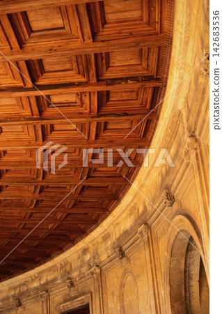 Intricate wooden coffered ceiling with light brown stone wall featuring arches and decorative elements Intricate wooden coffered ceiling with light brown stone wall featuring arches and decorative elements 142683536