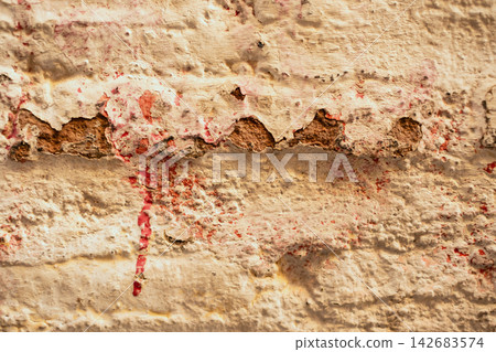 Weathered wall texture showing cracks, peeling beige paint, and decaying red bricks, creating an aged abstract background Weathered wall texture showing cracks, peeling beige paint, and decaying red bricks, creating an aged abstract background 142683574