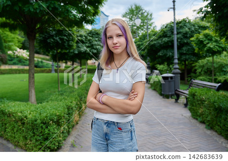 Teenage girl standing arms crossed in park with purple hair strands looking at camera Teenage girl standing arms crossed in park with purple hair strands looking at camera 142683639