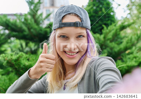 Teenage girl taking selfie showing thumbs up gesture outdoors close up Teenage girl taking selfie showing thumbs up gesture outdoors close up 142683641