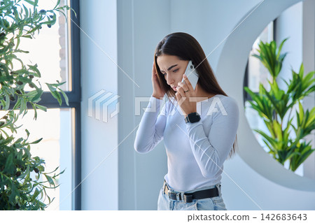 Shocked young woman speaking on smartphone with open mouth indoors Shocked young woman speaking on smartphone with open mouth indoors 142683643