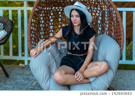 Young woman relaxing in woven hanging chair on sunny patio Young woman relaxing in woven hanging chair on sunny patio 142683683