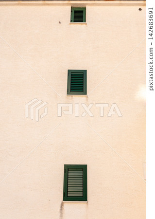Minimal beige building facade with three green shuttered windows Minimal beige building facade with three green shuttered windows 142683691