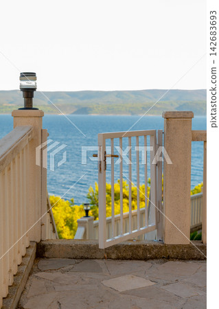 Open white gate overlooking a calm sea and distant hills Open white gate overlooking a calm sea and distant hills 142683693