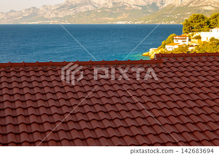 Red tiled roof overlooking blue sea and distant mountains Red tiled roof overlooking blue sea and distant mountains 142683694