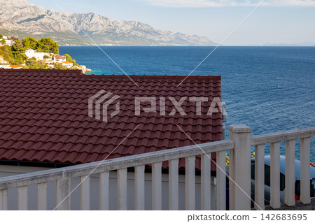 Red tiled rooftop overlooking calm blue sea and distant mountains Red tiled rooftop overlooking calm blue sea and distant mountains 142683695