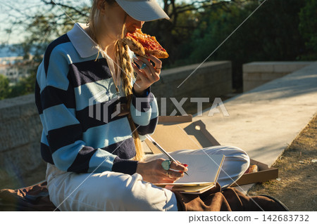 Casual outdoor pizza picnic while journaling in the park during golden hour Casual outdoor pizza picnic while journaling in the park during golden hour 142683732