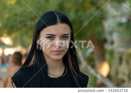 Serious young woman with dark hair standing outdoors in park Serious young woman with dark hair standing outdoors in park 142683738