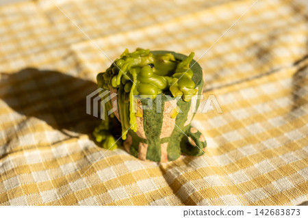 Green candle with drips on yellow checkered cloth in sunlight Green candle with drips on yellow checkered cloth in sunlight 142683873