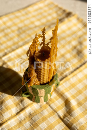 Artisan beeswax candle with rustic melting design on checkered cloth background Artisan beeswax candle with rustic melting design on checkered cloth background 142683874