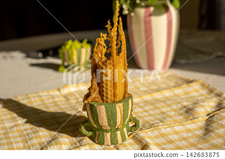 Rustic candle display in striped pot on checkered tablecloth with plants in sunlight Rustic candle display in striped pot on checkered tablecloth with plants in sunlight 142683875